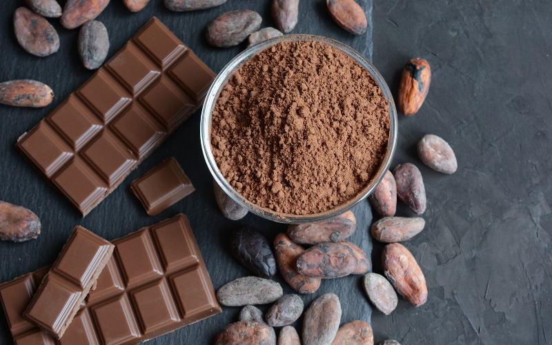 Ciotola piena di cacao in polvere circondata da tavolette di cioccolato e fave di cacao